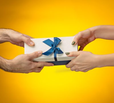 The closeup picture of man and woman's hands with gift box on yellow background