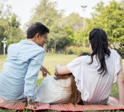 Behind Asian family are sit playing on the mat in the park.